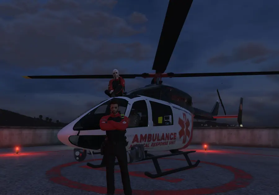 An ambulance helicopter on its helipad at dusk with two medics in front